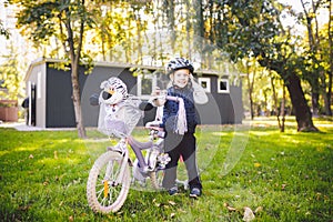 Funny child Caucasian girl blonde in a bicycle helmet near a purple bike with a basket in outside the park on a green