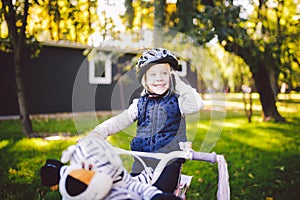 Funny child Caucasian girl blonde in a bicycle helmet near a purple bike with a basket in outside the park on a green