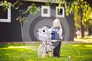 Funny child Caucasian girl blonde near a purple bike with a basket and a zebra toy in an outside park on a green lawn grass cart