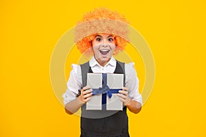 Funny child clown in wig and gift. Child with gift present box on isolated studio background. Gifting for kids birthday