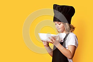 Funny child cook with cooking plate. Excited chef cook. Child wearing cooker uniform and chef hat preparing food, studio