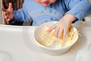 Funny child eating a grated apple with his hand from a plate, close-up.