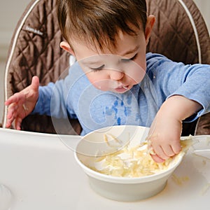 Funny child eating a grated apple with his hand from a plate, close-up.