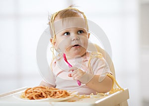 Funny child eating noodle. Grimy kid eats spaghetti with fork sitting on table at home