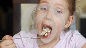 Funny child eats omelet in several pieces close up. Baby girl is hungry and has great appetite. Concept of home food and