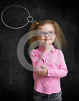 Funny child in eyeglasses standing near school chalkboard