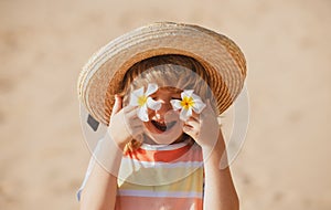 Funny child face close up. Kids in straw hat with eyes flower, summer portrait. Summer holiday. Covers eyes with flower