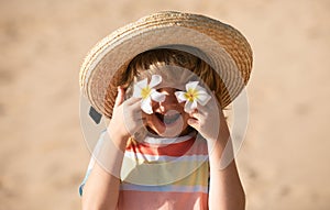 Funny child face close up. Kids in straw hat with eyes flower, summer portrait. Summer holiday. Covers eyes with flower