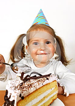 Funny child girl with birthday hat eating cake