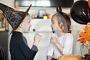 Funny child girl and boy in witch and evil costumes for Halloween eating candies lolly pops and have fun.