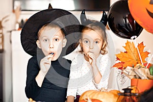 funny child girl and boy in witch and evil costumes for Halloween eating candies lolly pops and have fun.
