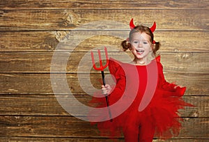 Funny child girl in devil halloween costume on dark wooden back