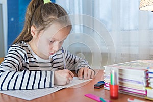 a funny child girl doing homework writing and reading at home