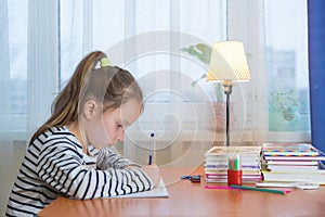 A funny child girl doing homework writing and reading at home