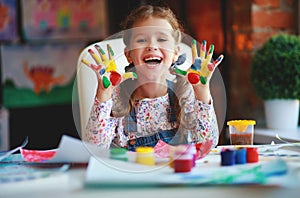 Funny child girl draws laughing shows hands dirty with paint