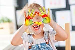 Funny child girl draws laughing shows hands dirty with paint