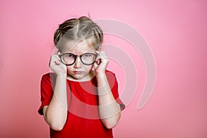Funny child girl in glasses against pink colored background. School kid is nerd and smart. Pupil afraid to do mistake