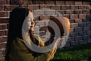 Funny child girl in orange pullover for Halloween with pumpkin and on a dark brick background