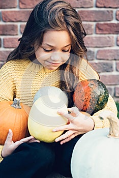 Funny child girl in orange pullover for Halloween with pumpkin and on a dark brick background