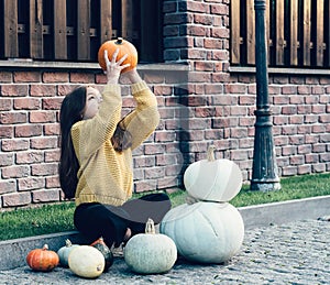 Funny child girl in orange pullover for Halloween with pumpkin and on a dark brick background