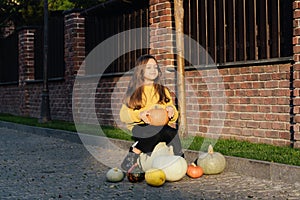 Funny child girl in orange pullover for Halloween with pumpkin and on a dark brick background