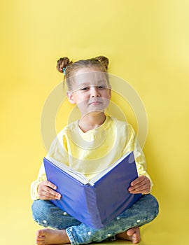 Funny child girl yellow jacket on a yellow background, sitting, reading a book, development and school concept