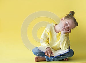 Funny child girl yellow jacket on a yellow background, sitting, reading a book, development and school concept
