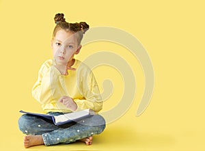 Funny child girl yellow jacket on a yellow background, sitting, reading a book, development and school concept