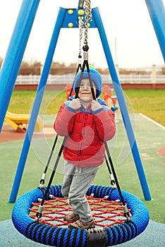 Funny child having fun with modern swing. Little boy playing on outdoor playground. Happy kid swinging on cold autumn day. Active