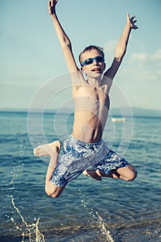 Funny child playing in sea splashing water and jumping.