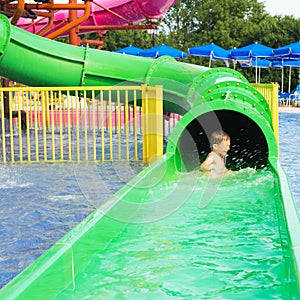 Funny child playing in water park splashing water. Summer holidays concept. Boy has into pool after going down water slide on sum