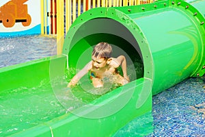 Funny child playing in water park splashing water. Summer holidays concept. Boy has into pool after going down water slide during