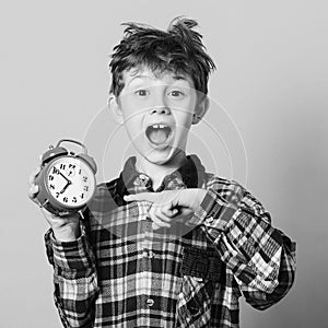 Funny child pointing at alarm clock. Excited boy overslept before school. Child back to school. Isolated on yellow. Education and