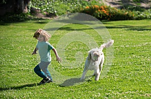 Funny child run with dog. Happy kid boy playing with dog in garden. Child runnin with a dog in park.