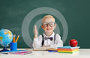 Funny child   schoolboy    student  raises his hand up near school blackboard