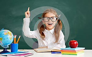 Funny child   schoolgirl    student  raises his hand up near school blackboard