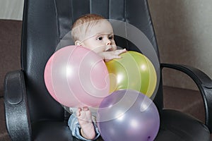Funny child sitting on chair little boy having fun playing big colored balloons