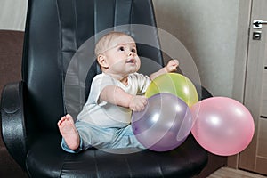 Funny child sitting on chair little boy having fun playing big colored balloons