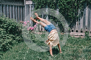 Funny child teenage girl doing cartwheel on a backyard. Excited joyful kid playing outdoor. Happy lifestyle childhood and freedom