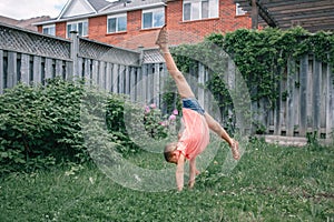 Funny child teenage girl in a red t-shirt doing cartwheel on backyard. Excited joyful kid playing outdoor. Happy lifestyle