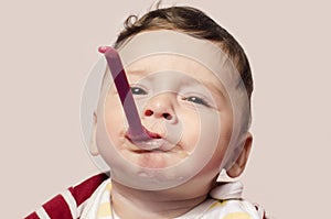 Funny child trying to feed himself baby food holding the spoon in the mouth.