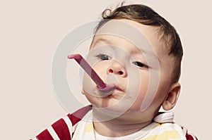 Funny child trying to feed himself baby food holding the spoon in the mouth.