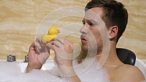 Funny childish male playing with rubber duck and pretend shooting it, leisure