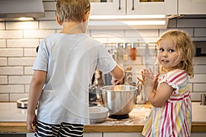 Funny children cooking homemade pastry dessert at modern kitchen spending time together
