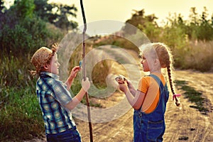 Funny children go fishing in the summer evening on a dirt road