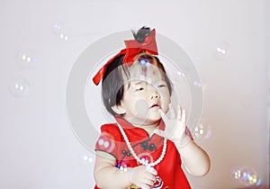 Funny Chinese little baby in red cheongsam play soap bubbles