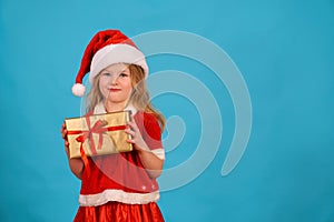 Funny Christmas child girl in santa claus cap is hold gift grimacing. Play with facial expressions. Sly look of a