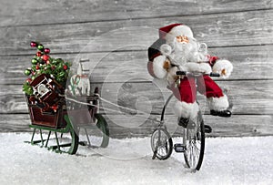 Funny christmas greeting card with Santa on a bike pulling a slide.