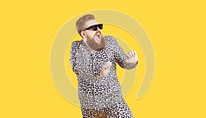 Funny chubby guy in cool sunglasses and leopard pajamas dancing isolated on yellow background