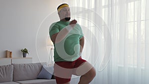 Funny chubby man in sports clothes working out at home, running in place, slow motion
